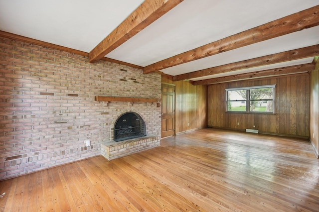 unfurnished living room with light wood finished floors, beamed ceiling, a brick fireplace, and wooden walls