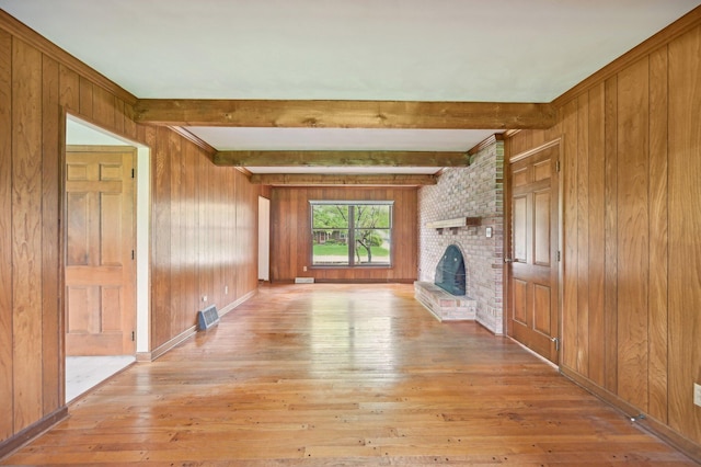unfurnished living room with light wood-type flooring, wood walls, a fireplace, and beamed ceiling