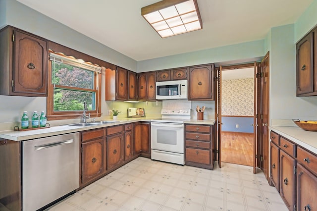 kitchen featuring white appliances, a sink, light floors, light countertops, and wallpapered walls