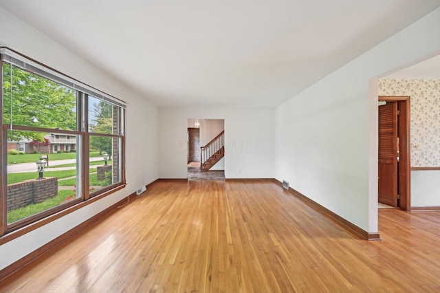 unfurnished living room with light wood-style floors, stairway, and baseboards