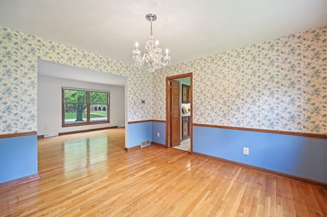 spare room featuring wallpapered walls, a chandelier, light wood-style floors, and baseboards