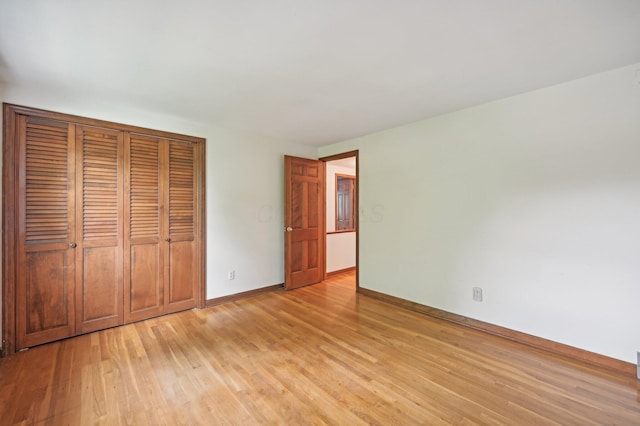 unfurnished bedroom with light wood-style flooring, a closet, and baseboards