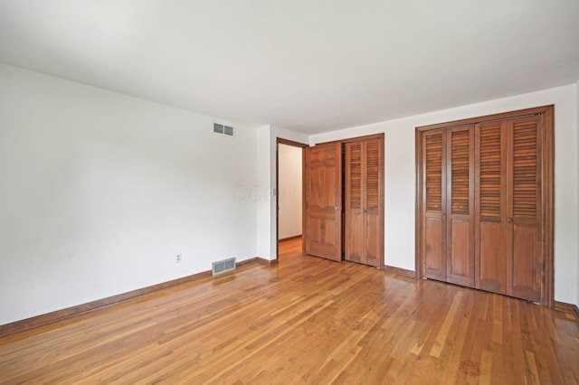 unfurnished bedroom featuring multiple closets, light wood-type flooring, and baseboards