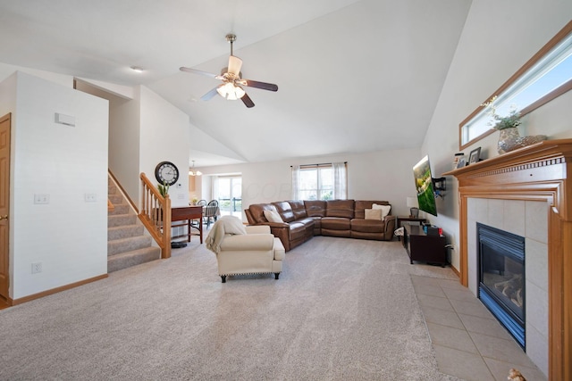 living area with ceiling fan, stairs, high vaulted ceiling, a tile fireplace, and light colored carpet