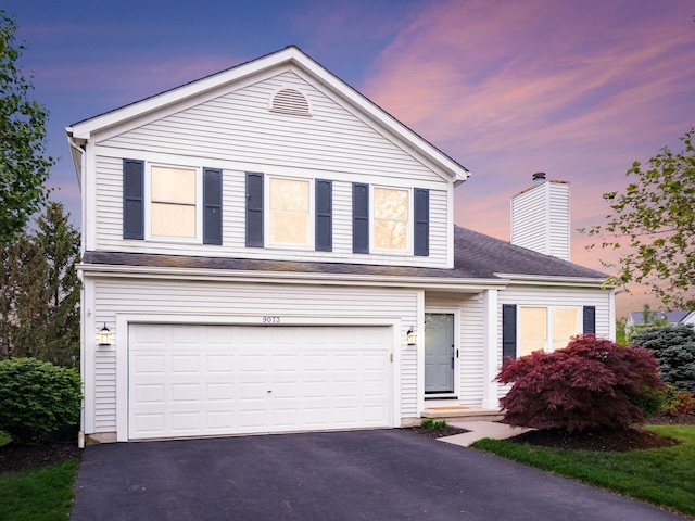traditional-style house featuring roof with shingles, a chimney, and aphalt driveway