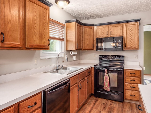 kitchen featuring a sink, wood finished floors, a textured ceiling, black appliances, and light countertops