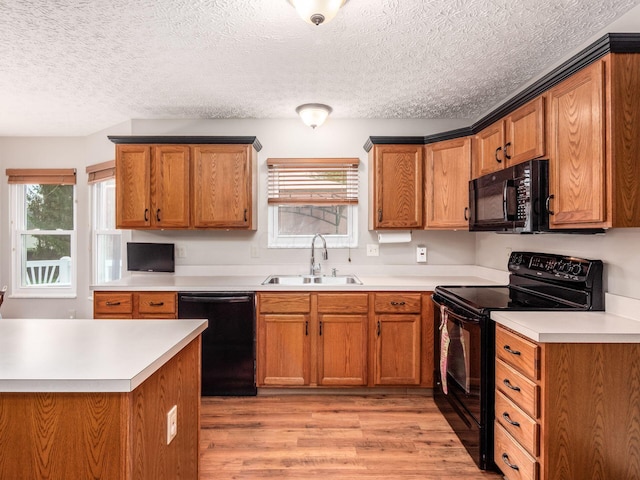 kitchen featuring light countertops, light wood-style flooring, black appliances, and a sink