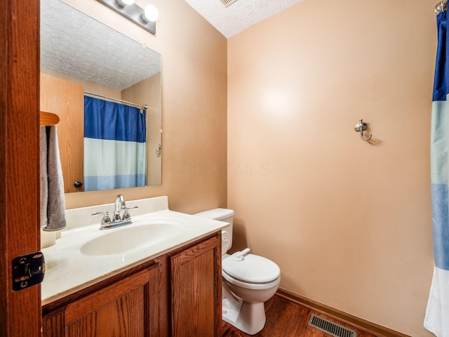 bathroom with toilet, wood finished floors, a textured ceiling, visible vents, and vanity