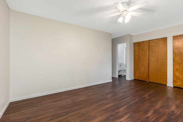 unfurnished bedroom featuring dark wood-style flooring, multiple closets, baseboards, and a ceiling fan