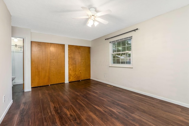 unfurnished bedroom featuring wood finished floors, multiple closets, baseboards, and a ceiling fan