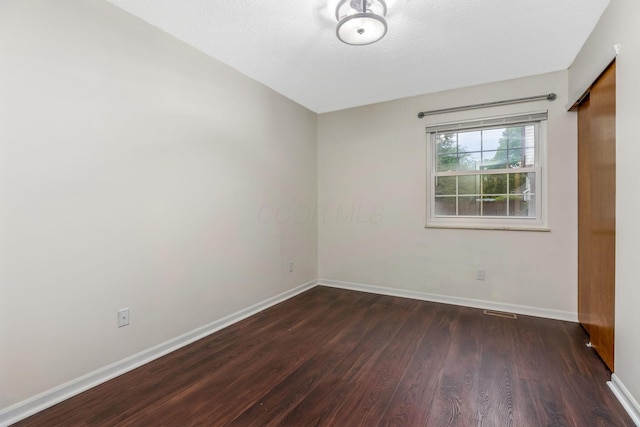 empty room with dark wood-type flooring, baseboards, and a textured ceiling