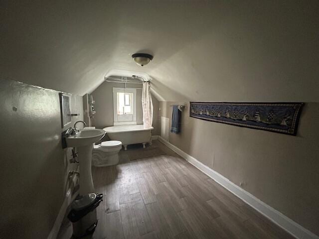 full bathroom with lofted ceiling, toilet, wood finished floors, baseboards, and a bath
