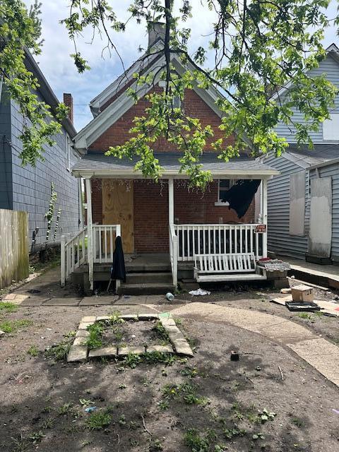 back of house featuring a porch, fence, and brick siding