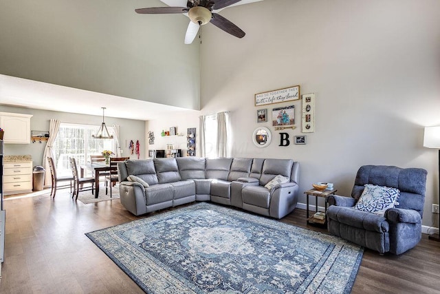 living area featuring a towering ceiling, baseboards, wood finished floors, and ceiling fan with notable chandelier