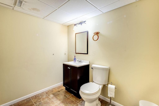 bathroom featuring toilet, vanity, visible vents, a drop ceiling, and baseboards