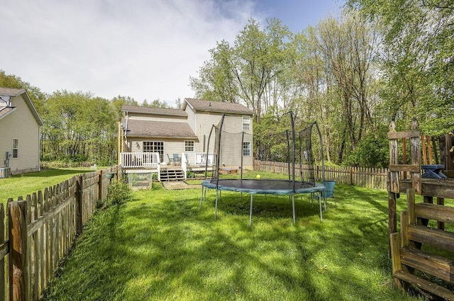 rear view of house featuring a fenced backyard, a wooden deck, a trampoline, and a yard
