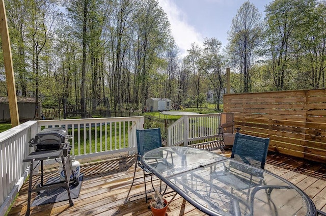 wooden terrace featuring a yard, an outbuilding, outdoor dining space, fence, and a storage shed