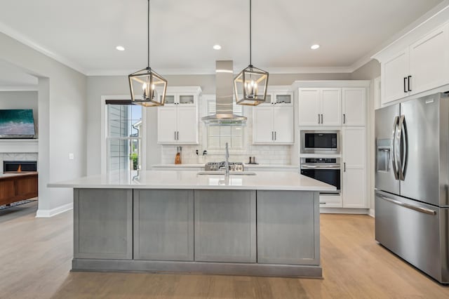 kitchen with appliances with stainless steel finishes, ventilation hood, decorative backsplash, light countertops, and a center island with sink