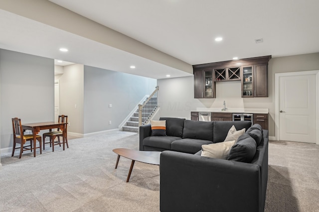 living room featuring light colored carpet, bar with sink, recessed lighting, stairs, and baseboards