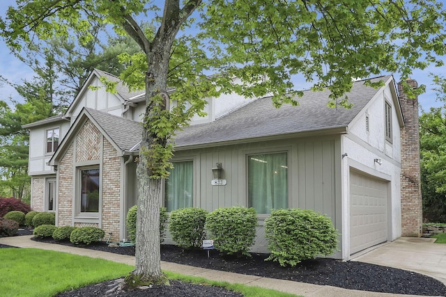 view of front of home featuring an attached garage, a chimney, roof with shingles, brick siding, and driveway