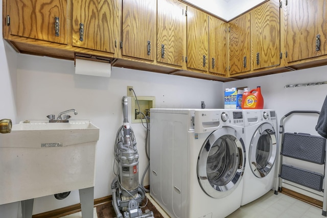 clothes washing area with cabinet space, light floors, washer and dryer, and a sink