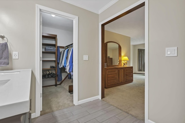 hallway featuring crown molding, light carpet, baseboards, and wood finish floors