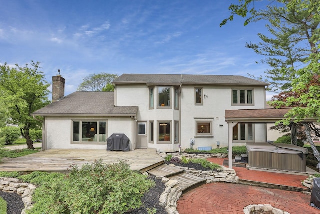 back of house with a hot tub, stucco siding, a chimney, and a wooden deck