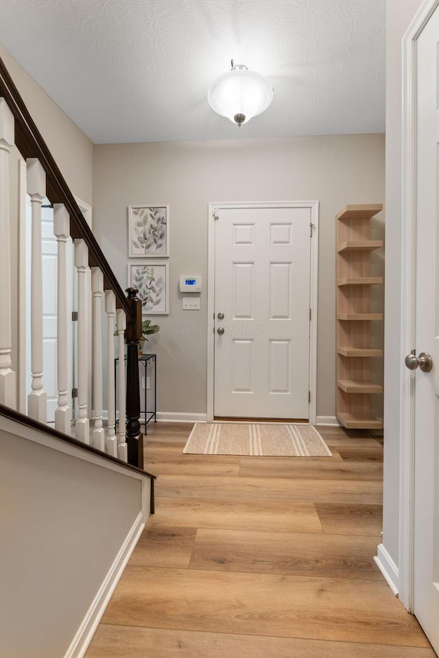foyer featuring stairway, light wood-style floors, and baseboards