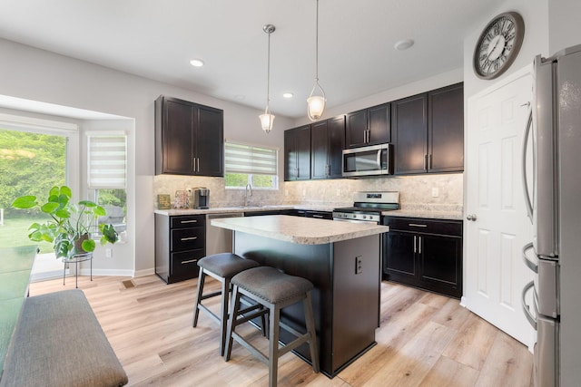 kitchen featuring appliances with stainless steel finishes, light wood finished floors, a breakfast bar, light countertops, and tasteful backsplash