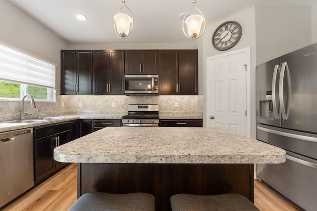kitchen featuring appliances with stainless steel finishes, a sink, light countertops, tasteful backsplash, and light wood-style floors