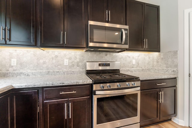 kitchen with appliances with stainless steel finishes, tasteful backsplash, light stone countertops, dark brown cabinetry, and light wood finished floors