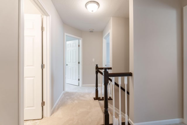 hall featuring an upstairs landing, light colored carpet, and baseboards