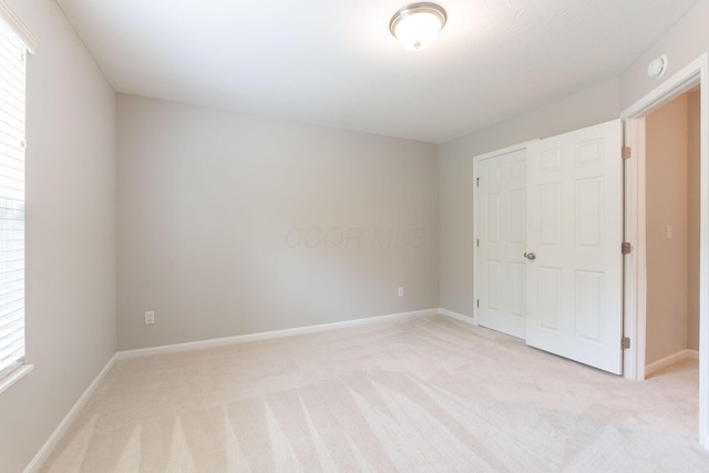 unfurnished bedroom featuring light carpet, a closet, and baseboards