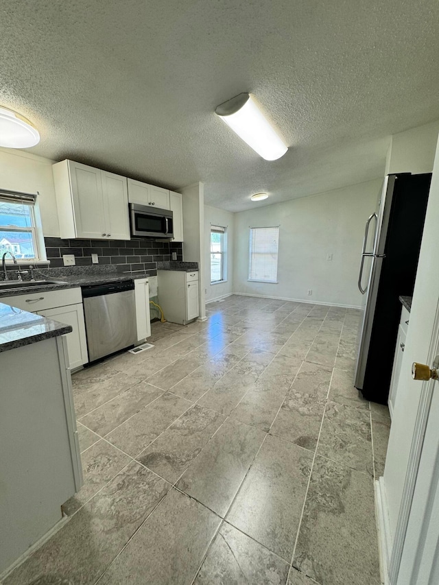 kitchen featuring a sink, white cabinets, a textured ceiling, appliances with stainless steel finishes, and decorative backsplash