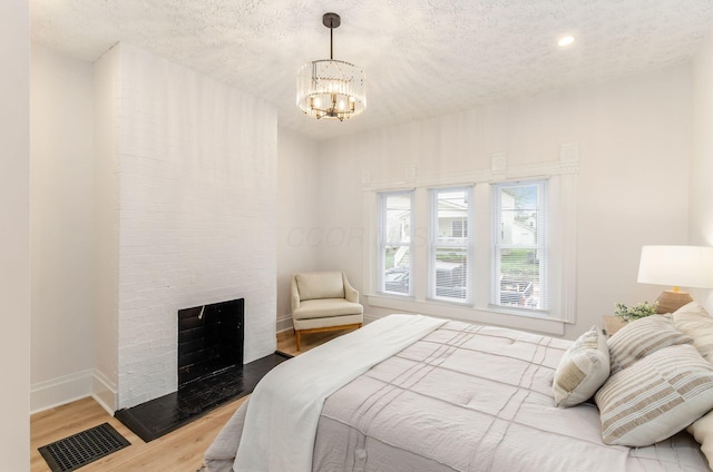 bedroom with wood finished floors, a fireplace, visible vents, baseboards, and a chandelier
