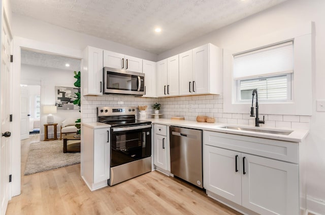 kitchen with a sink, light wood-type flooring, backsplash, light countertops, and appliances with stainless steel finishes