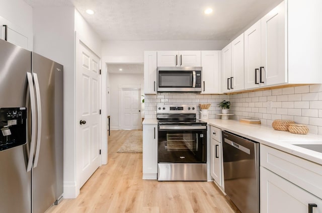 kitchen with recessed lighting, light wood finished floors, decorative backsplash, light countertops, and appliances with stainless steel finishes