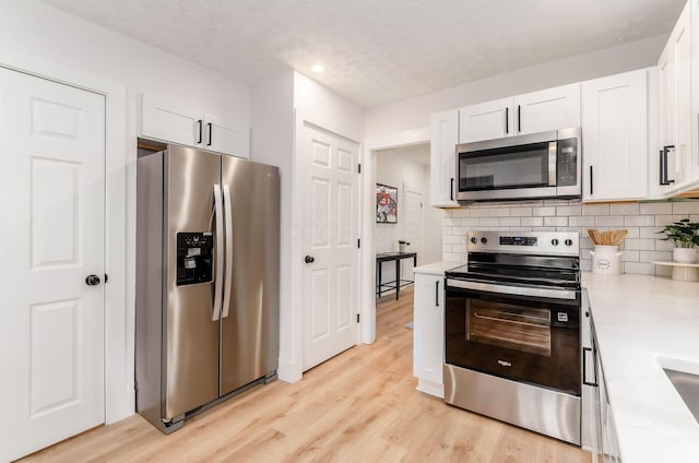 kitchen featuring white cabinetry, stainless steel appliances, light wood-style flooring, and a textured ceiling