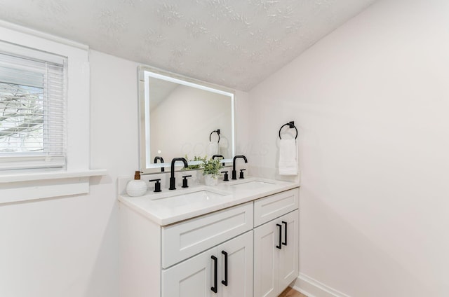 bathroom with double vanity, a textured ceiling, vaulted ceiling, and a sink