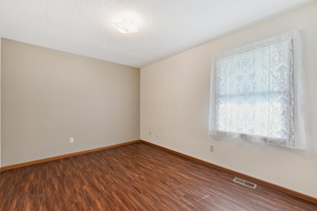 unfurnished room with visible vents, baseboards, and dark wood-type flooring