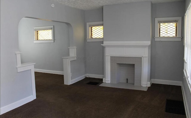 unfurnished living room with dark colored carpet, baseboards, a fireplace with flush hearth, and visible vents