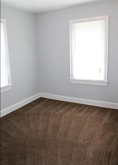 empty room featuring baseboards, dark carpet, and a wealth of natural light