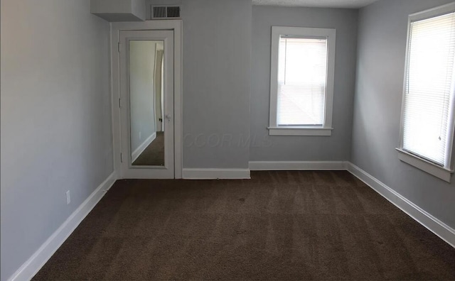 unfurnished room with baseboards, dark colored carpet, and visible vents