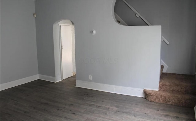 interior space featuring stairway, arched walkways, baseboards, and wood finished floors
