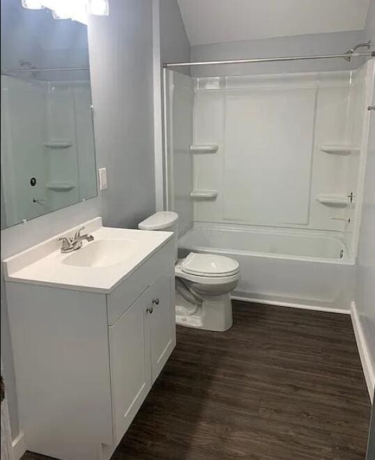 bathroom featuring lofted ceiling, toilet, vanity, tub / shower combination, and wood finished floors