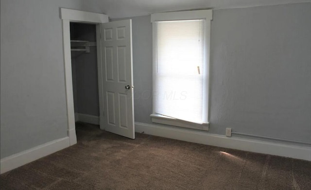 unfurnished bedroom with a closet, dark colored carpet, and baseboards
