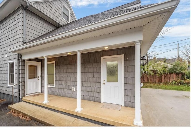 entrance to property featuring roof with shingles and fence