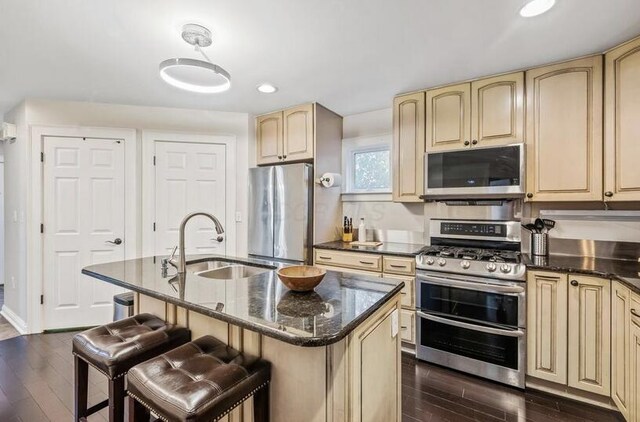 kitchen with cream cabinets, appliances with stainless steel finishes, a sink, and dark wood-type flooring