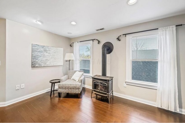 sitting room featuring a wood stove, hardwood / wood-style flooring, baseboards, and visible vents