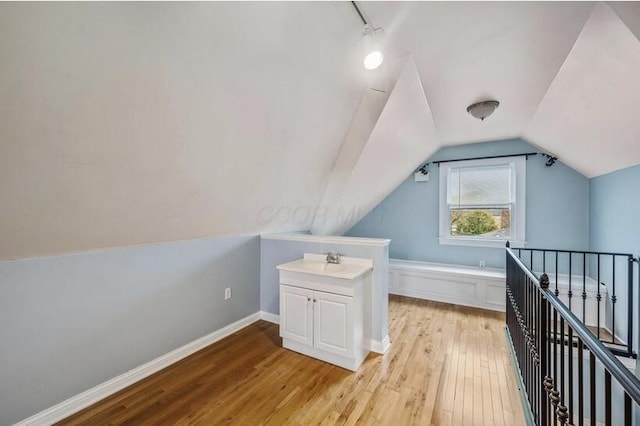 bonus room with a sink, vaulted ceiling, light wood-style flooring, and baseboards